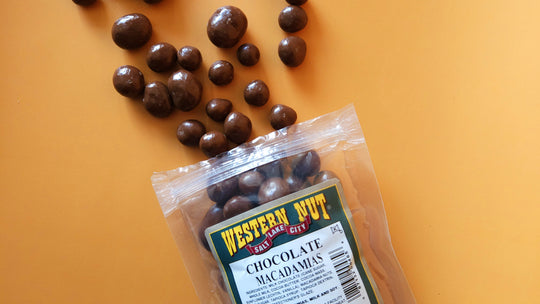 A luxurious assortment of macadamia chocolates and various nuts on a rustic wooden table, surrounded by handcrafted brittles and fudges in warm, earthy tones.
